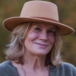 head and shoulders bio photo of Kirsten, light color hat, dark color shirt, nature blurred background